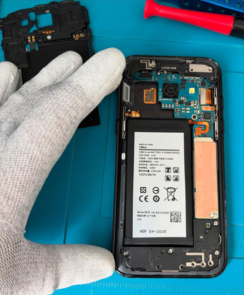 Téléphone ouvert sur un tapis de réparation, à côté d’une main gantée
